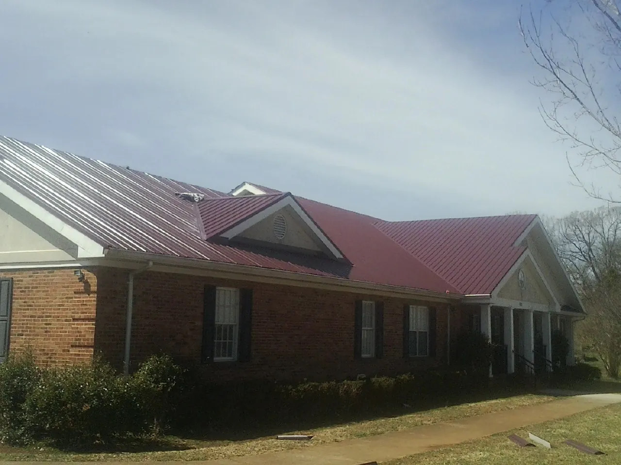 Red metal roof with gabled entries on a long brick building, from a Hail Damage Roof Repair job in Goldens Bridge