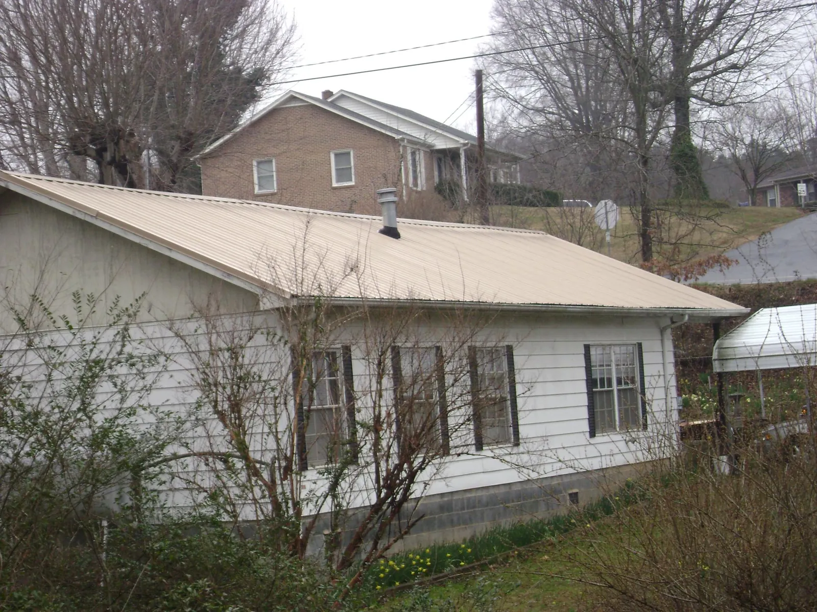 Tan metal roof on a white sided house set into a hillside — Commercial Roofing by Roofing Brothers in Goldens Bridge