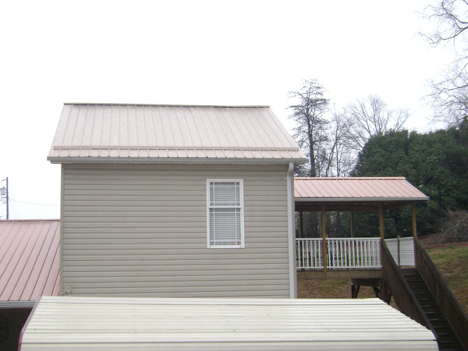 Tan metal roofs on a two story addition and attached porch, from a Roof Replacement job in Goldens Bridge